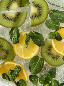 Vibrant citrus and kiwi slices with mint leaves in a sparkling beverage viewed from above.